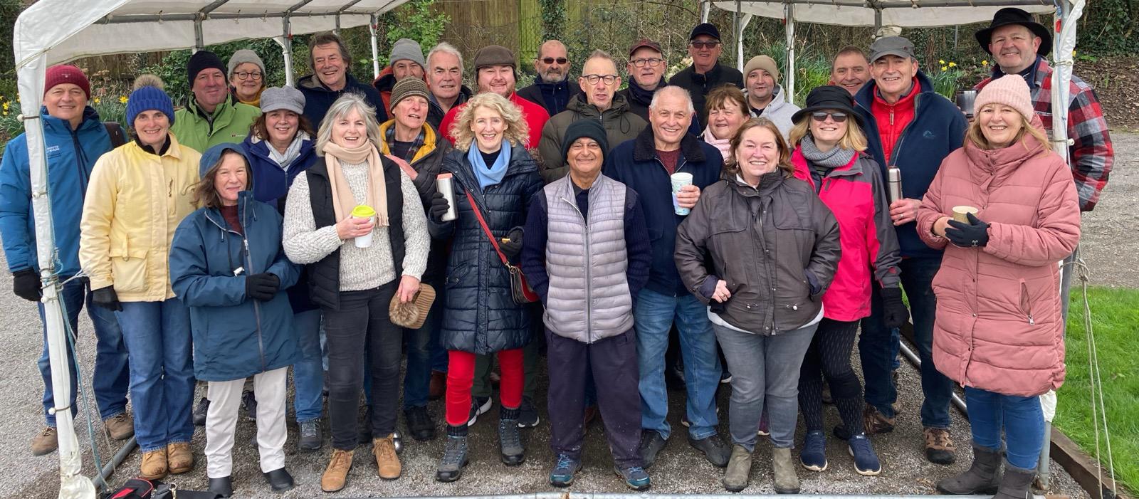 Around thirty club members in winter coats standing together under the gazebo beside the pistes